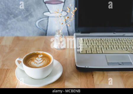 Une tasse de café latte art coeur sur table en bois, avec un ordinateur portable. Banque D'Images