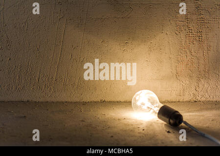 La photo en gros plan de l'ampoule électrique se trouvant sur le plancher brillant sur mur gris plâtre frais présentant des lésions. L'électricité et la réparation. Banque D'Images