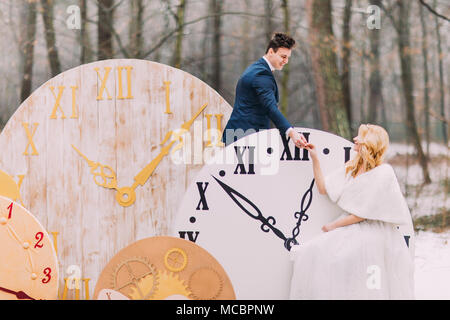 Happy wedding couple holding hands at doucement les grandes horloges vintage en forêt d'automne. Décorations créatives Banque D'Images