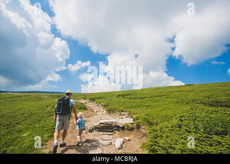 Père et fils de la randonnée dans les montagnes de Rila, Bulgarie. Un voyageur et un petit garçon sont à pied le long de la route se tenant la main. retour voir les nuages blancs énormes. Banque D'Images