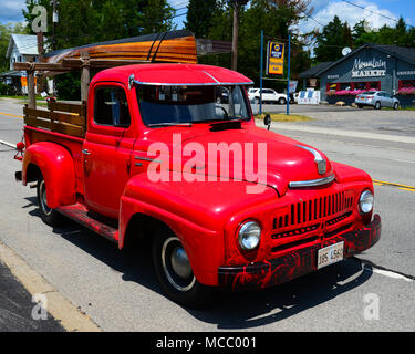 Un rouge lumineux vintage 1951 International ère camionnette ou camion sur le bord de la route en spéculateur, NY USA haler un canot en bois construit sur mesure. Banque D'Images