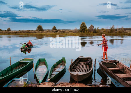 Dobrush, Bélarus - 25 juillet 2013 : Les Enfants du Bélarus de pêche en bois vieux bateaux à rame en été Coucher du Soleil Banque D'Images