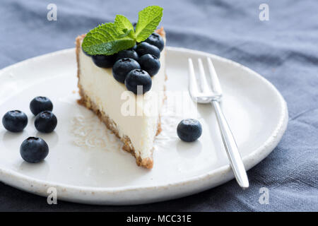 Tranche de gâteau au fromage avec des bleuets frais et feuille de menthe sur plaque blanche. Vue rapprochée Banque D'Images