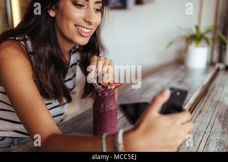 Prendre une femme avec un smoothie selfies en utilisant un téléphone mobile pour son blog. Prise de photos pour l'alimentation blogger son blog à la maison. Banque D'Images