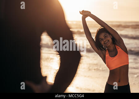 Femme dans l'exercice de sport à la plage avec son entraîneur. Athletic woman working out à la plage le matin. Banque D'Images