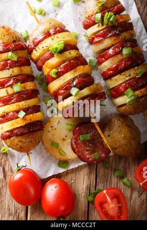 Grillades barbecue Brochettes de pommes de terre chaudes avec salami saucisses et l'oignon vert gros plan sur la table. Haut Vertical Vue de dessus Banque D'Images