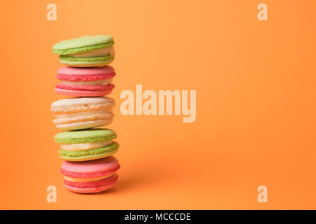 Macarons colorés rangée sur fond orange. Composition éparse with copy space Banque D'Images