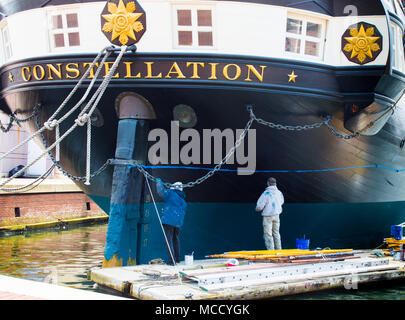 2 travailleurs sur une plate-forme flottante peinture l'extérieur de l'USS Constellation historique dans l'arrière-port de Baltimore Banque D'Images