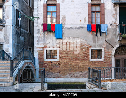 Old Venetian typique façade de briques rouges et de ciment avec des vêtements colorés devant les fenêtres au-dessus d'un canal traditionnel avec une gondole dock Banque D'Images