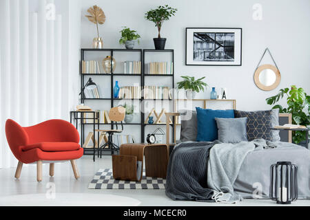 Fauteuil orange à côté de la table en bois et gris lit dans chambre à coucher intérieur avec des plantes et de l'affiche Banque D'Images