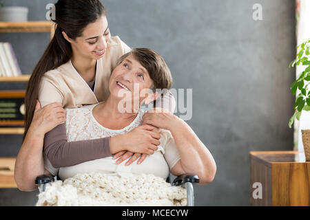 Smiling caregiver hugging her senior patient in a wheelchair Banque D'Images