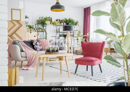 Fauteuil rouge debout par une table de bois blanc à l'intérieur chambre avec canapé et plantes Banque D'Images