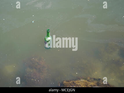 Flacon en verre vert flotte dans l'eau sale et pollue l'environnement Banque D'Images