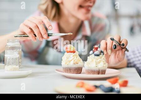 Méconnaissable pâtissiers femelle decorating cupcakes crème délicieux avec les baies fraîches et glaçage, close-up view Banque D'Images