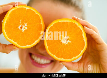 Happy young woman holding deux tranches d'orange en face des yeux Banque D'Images
