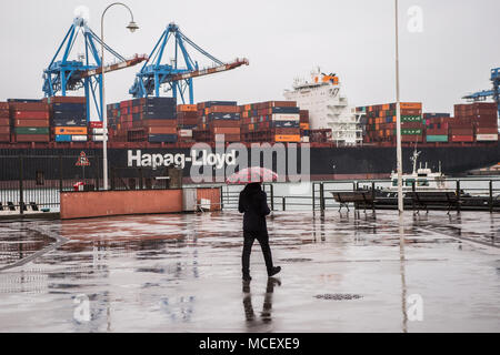 Un homme qui marche sous la pluie en face de Hapag Lloyd Express Hanovre loading à Gênes, Italie (GOA) Banque D'Images