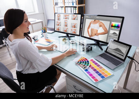 Happy Young Female Designer travaillant avec des photographies sur plusieurs ordinateurs sur le lieu de travail Banque D'Images