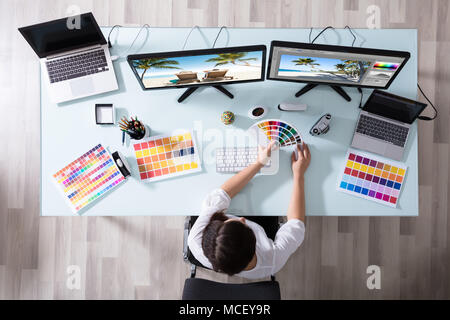 High Angle View of a female Designer en utilisant un échantillon de couleur tout en travaillant sur plusieurs ordinateurs Banque D'Images