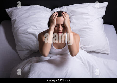 Young Woman Sitting on Bed souffrant de maux de tête Banque D'Images
