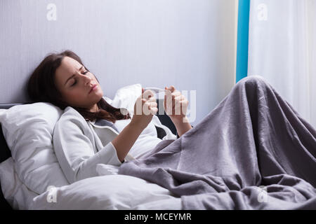 Sick Young Woman Lying On Bed contrôle la température du corps avec le thermomètre Banque D'Images