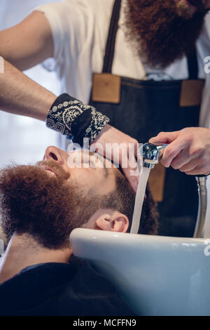 Gros plan des mains d'un coiffeur qualifié donnant un lavage des cheveux au client Banque D'Images