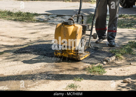 Les détails de la réparation des routes. Un travailleur avec un pavé manuel aligne l'asphalte chaud sur la route. Banque D'Images