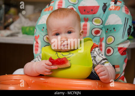 bébé garçon de 12 mois aux cheveux rouges dans une chaise haute manger Banque D'Images