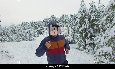 Jeune homme de runner Sportsman qui traverse la forêt enneigée. shot Vue de face hiver arbre forêt dans la neige Banque D'Images