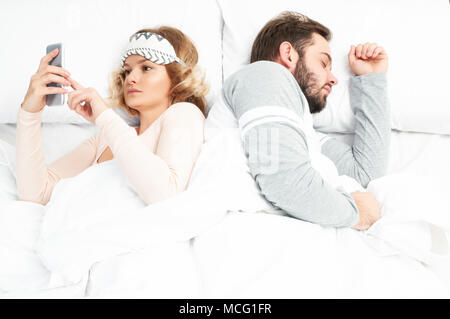 Femme en utilisant son téléphone dans le lit pendant que son mari est en train de dormir à côté d'elle Banque D'Images