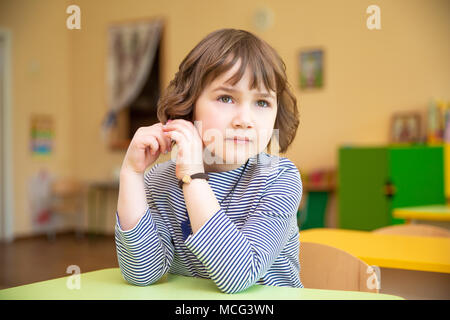 Portrait of cute little Girl with hands clasped sitting at desk in classroom Banque D'Images