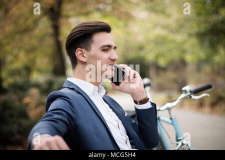 Young attractive businessman talking on smartphone à l'extérieur dans le parc Banque D'Images