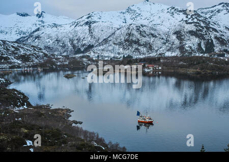 Bateau de pêcheur de partir dans un fjord norvégien en hiver entouré de montagnes Banque D'Images