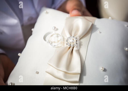 Les anneaux de mariage sur l'oreiller blanc retenus dans les mains Banque D'Images