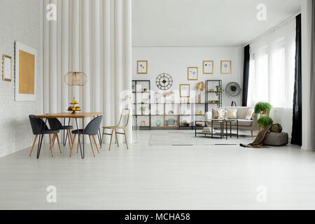 Chaises table à manger à l'intérieur de l'espace ouvert lumineux avec canapé et d'or de la peinture sur mur blanc Banque D'Images