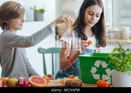 Fille et garçon trowing hors fruits les déchets en conteneurs de recyclage vert Banque D'Images