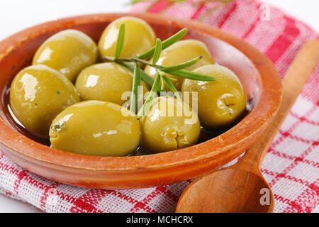 Bol d'olives vertes avec le romarin et cuillère en bois sur le torchon à carreaux - détail Banque D'Images