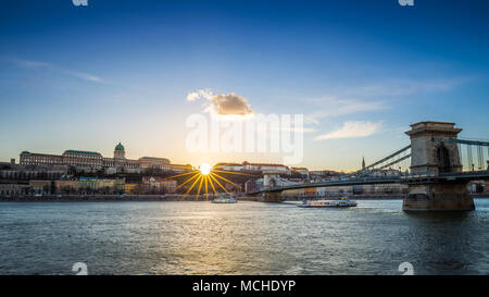 Budapest, Hongrie - des bateaux touristiques sur Danube au coucher du soleil avec le pont à chaînes Széchenyi et le château de Buda Palais Royal. Ciel bleu clair. Banque D'Images