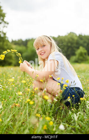 Fille blonde picks fleurs de pissenlit au printemps sur un pré Banque D'Images