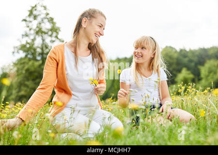 La mère et la fille sont assis dans l'herbe et la cueillette des fleurs ensemble Banque D'Images