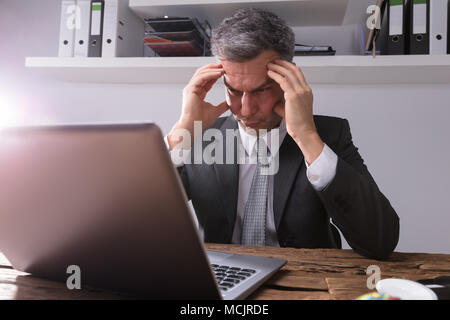 Upset Businessman Sitting in Office avec un ordinateur portable sur un bureau en bois Banque D'Images