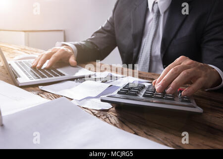 Close-up de l'homme d'affaires à l'aide de la main de calculatrice sur un bureau en bois Banque D'Images