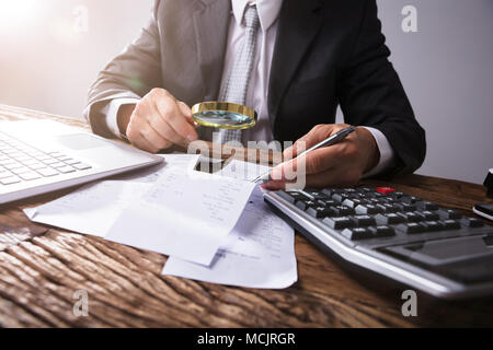 Close-up de la main de l'homme d'affaires à la loupe par les reçus au travail à Banque D'Images