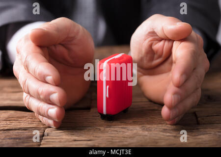 Close-up de l'homme d'affaires's Hand Holding Red Suitcase sur bureau en bois Banque D'Images