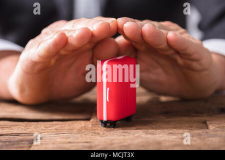 Close-up de l'homme d'affaires's Hand Holding Red Suitcase sur bureau en bois Banque D'Images