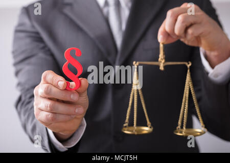 Close-up d'un juge's Hand Holding Red paragraphe symbole et l'échelle de la Justice Banque D'Images