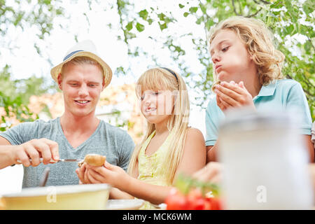 Coups de père du beurre sur une baguette tout en prenant le petit déjeuner avec les enfants dans le jardin Banque D'Images