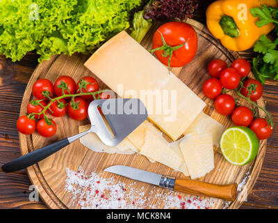 Vue d'en haut. planche en bois avec fromage parmesan, tomates cerises fraîches, de la laitue, sel de mer, de la chaux, le paprika et le poivre. bulgare rouge Le couteau pour couper les légumes. La vie toujours appétissants Banque D'Images