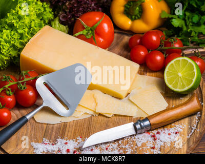 Vue d'en haut. planche en bois avec fromage parmesan, tomates cerises fraîches, de la laitue, sel de mer, de la chaux, le paprika et le poivre. bulgare rouge Le couteau pour couper les légumes. La vie toujours appétissants Banque D'Images