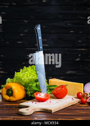 La vie toujours appétissante. Poivron jaune bulgare frais, tomates cerises, feuilles de laitue, oignon rouge, fromage, basilic vert sur planche de bois. Le couteau pour couper les légumes. Banque D'Images