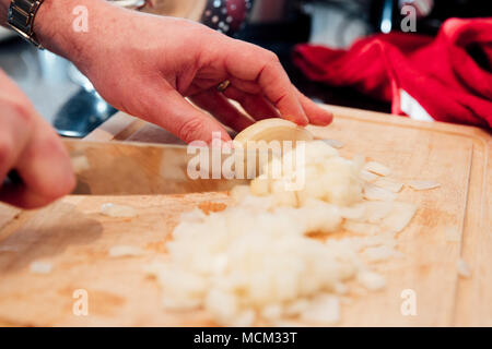 Gros plan d'un homme mûr de couper un oignon sur une planche à découper dans la cuisine de sa maison. Banque D'Images